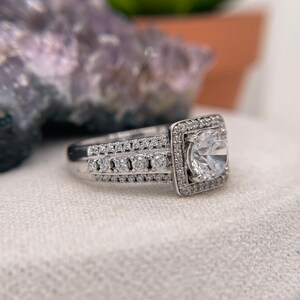 May include: A silver engagement ring with a large, round, clear center stone surrounded by smaller stones. The band is also set with smaller stones.