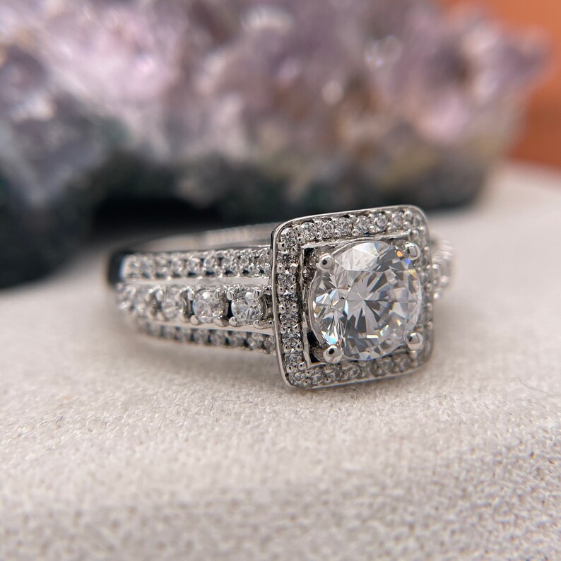 May include: A silver engagement ring with a large, round, clear center stone surrounded by a halo of smaller stones. The band is also set with smaller stones.