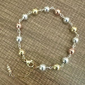 May include: A delicate bracelet featuring a series of small, round beads in silver, gold, and rose gold tones. The beads are strung together with fine silver wire, and the bracelet has a gold-colored clasp and extender chain.