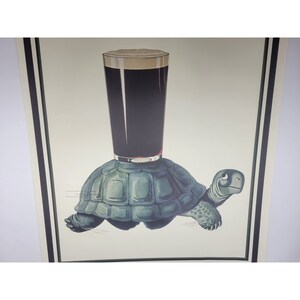 May include: A vintage illustration of a turtle carrying a glass of dark beer on its back. The turtle is green and the beer is dark brown with a white head of foam.