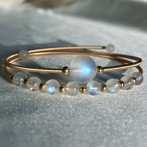 Op de afbeelding: Een gouden armband met een grote maansteenkraal en kleinere maansteenkralen. De armband is gemaakt van twee draden.