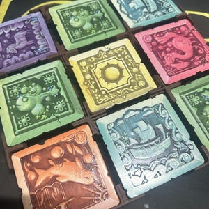 May include: A set of nine colourful square tiles with different illustrations. Each tile features a unique design, including a ship, a sun, a fish, and a unicorn. The tiles are made of a textured material and have a slightly raised border.