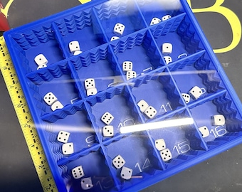 May include: A blue plastic tray with numbered compartments filled with white dice. The tray is open and the dice are visible.