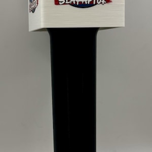 May include: A black handle attached to a white square top featuring a circular graphic of a blue raptor smoking a cigar with the text SEARAPTOR in red and white. The design includes a small wisp of smoke rising from the cigar above the raptor.