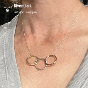 May include: A silver chain necklace with three interlocking rings. The rings are made of different metals: gold, silver, and rose gold.