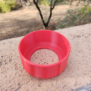 Pu&ograve; includere: Un anello di plastica rosso brillante stampato in 3D con una superficie liscia e arrotondata e un foro al centro.