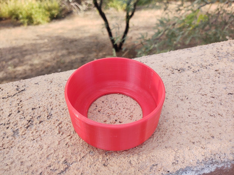 Pu&ograve; includere: Un anello di plastica rosso brillante stampato in 3D con una superficie liscia e arrotondata e un foro al centro.