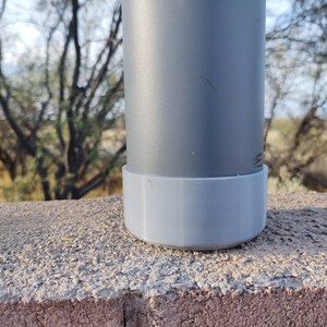 Pu&ograve; includere: Una bottiglia d'acqua in metallo grigio con una base in plastica grigia. La bottiglia &egrave; appoggiata su una superficie di cemento.