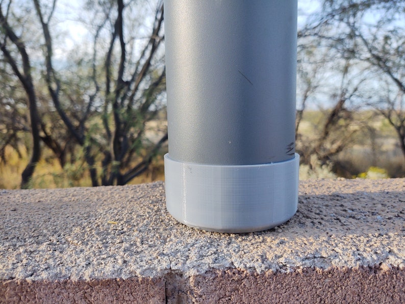 Pu&ograve; includere: Una bottiglia d'acqua in metallo grigio con una base in plastica grigia. La bottiglia &egrave; appoggiata su una superficie di cemento.