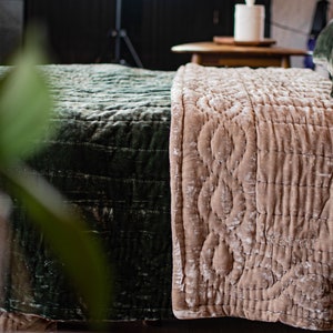 May include: A close-up of a bed with a green and beige quilted bedspread. The bedspread is made of a soft, velvety fabric and has a subtle pattern.
