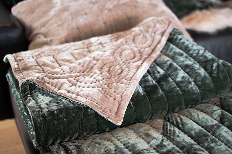 May include: A soft, quilted throw blanket in a deep green velvet with a light pink velvet top layer. The blanket is folded and displayed on a couch.