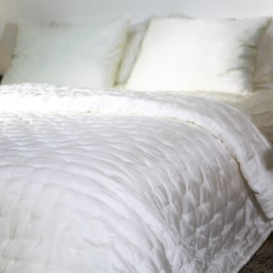 May include: A white quilted bedspread with a ruffled edge. The bedspread is made of soft, luxurious fabric and is perfect for adding a touch of elegance to any bedroom.