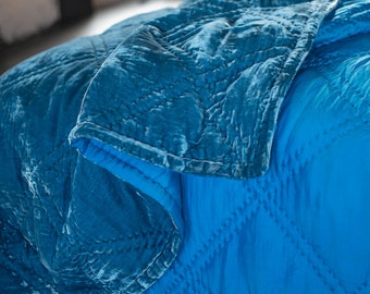 May include: A teal blue velvet quilt with a quilted pattern. The quilt is folded over itself and has a soft, luxurious feel.