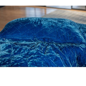 May include: A blue velvet quilted comforter and pillow set. The comforter is folded and the pillow is placed on top.