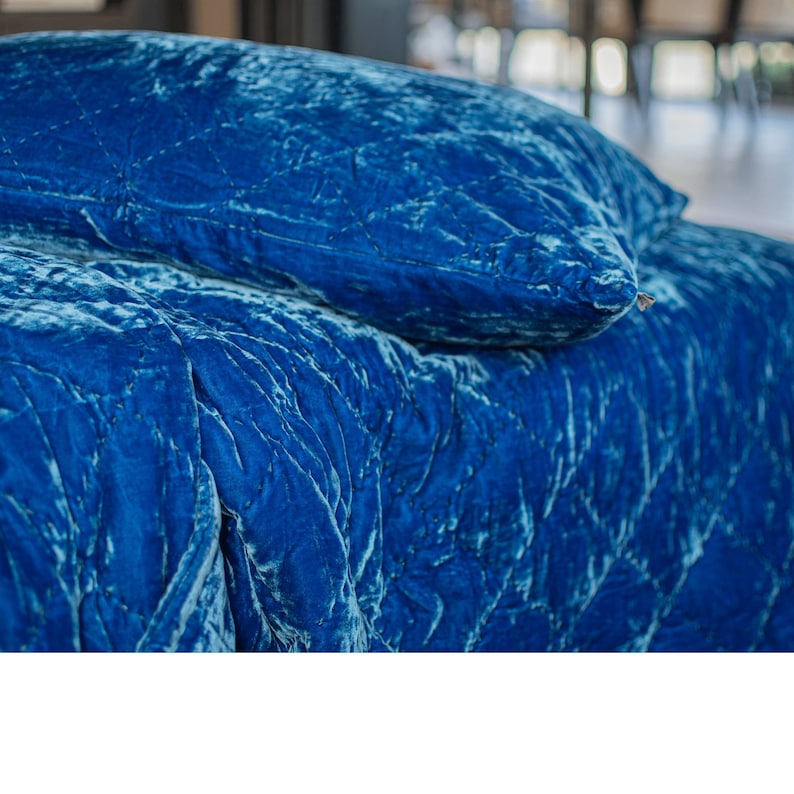May include: A close-up of a blue velvet quilted bedding set. The bedding is soft and luxurious, with a subtle sheen. The set includes a pillow and a duvet cover.