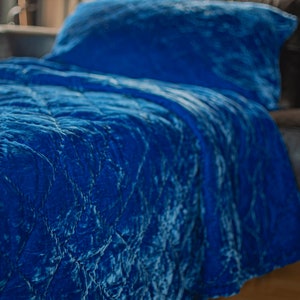 May include: A blue velvet quilted bedspread with a matching pillow. The bedspread has a crinkled texture and a soft, luxurious feel.