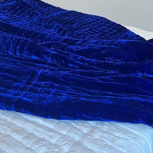 K&ouml;nnte beinhalten: Eine k&ouml;nigsblaue Samtdecke mit Steppmuster. Die Decke ist gefaltet und &uuml;ber ein wei&szlig;es Bett gelegt.