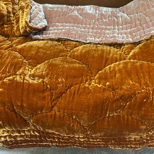 Może przedstawiać: Złoty welurowy koc pikowany z jasnoróżowym welurowym tyłem. Koc ma pikowany wzór z zaokrąglonych kształtów.