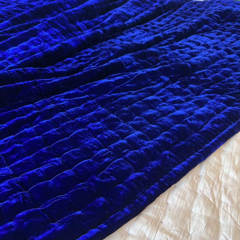 K&ouml;nnte beinhalten: Eine k&ouml;nigsblaue Samtdecke mit Steppmuster. Die Decke ist in der H&auml;lfte gefaltet und der Stoff ist weich und pl&uuml;schig.