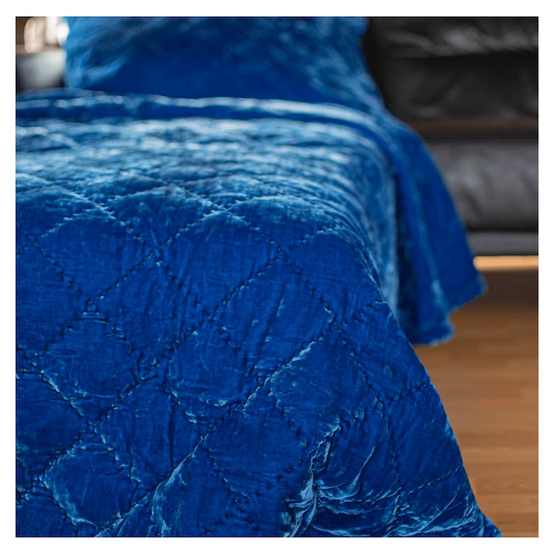 May include: A blue velvet quilted throw blanket with a diamond pattern. The blanket is folded and draped over a bed.