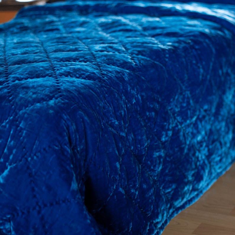 May include: A close-up of a blue velvet quilted blanket with a diamond pattern. The blanket is soft and luxurious, and it would be perfect for adding a touch of elegance to any bedroom.