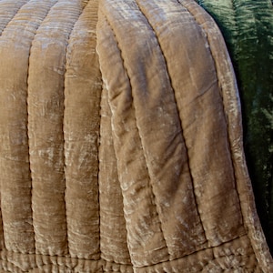 May include: A quilted throw blanket in a light brown color with a green velvet throw blanket folded on top. The throw blankets have a textured, crinkled look.