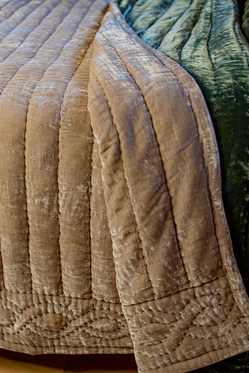 May include: A quilted throw blanket in a light brown color with a green velvet throw blanket folded on top. The throw blankets have a textured, crinkled look.