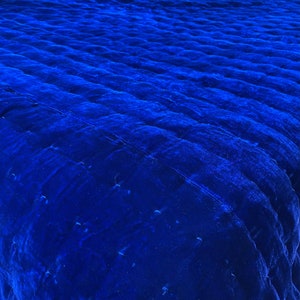 K&ouml;nnte beinhalten: Nahaufnahme eines tiefblauen, gesteppten Samtstoffes. Der Stoff hat eine weiche, pl&uuml;schige Textur und einen dezenten Glanz.