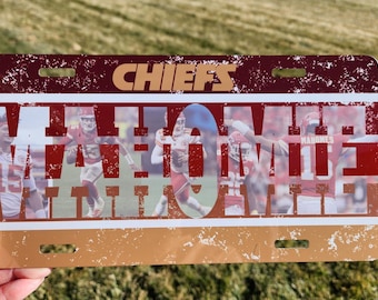 May include: A red, white, and gold metal license plate with the word "CHIEFS" in white letters and the word "MAYHEM" in white letters with a distressed look. The license plate has a photo of football players in red uniforms.