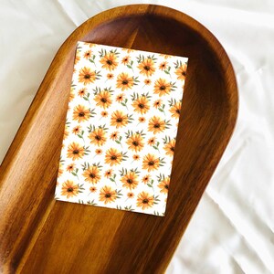 May include: A white card with a repeating pattern of orange and yellow flowers on a brown wooden tray.