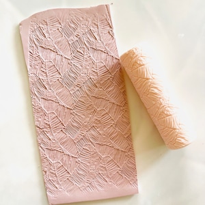 May include: A pink polymer clay roller with a leaf pattern and a sheet of pink polymer clay with the same leaf pattern embossed into it.