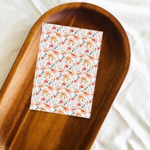 May include: A white card with a floral pattern featuring small orange and pink flowers on a white background. The card is sitting on a wooden tray.