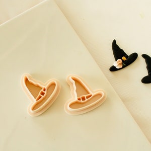 May include: Two plastic witch hat cookie cutters and two black fondant witch hats with pink flower accents.