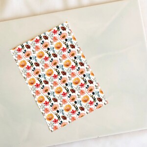 May include: A white background with a repeating pattern of watercolor flowers. The flowers are yellow, pink, and red with green leaves and brown pine cones.