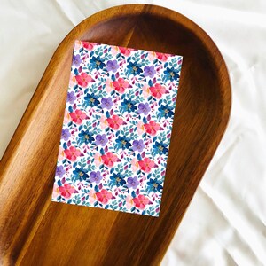 May include: A white card with a floral pattern featuring pink, blue, and purple flowers on a wooden tray.