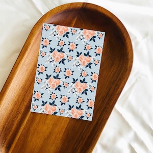 May include: A light blue card with a repeating pattern of peach-colored roses and white flowers. The roses have dark green leaves.