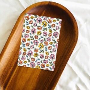 May include: A white card with a floral pattern featuring pink, orange, and yellow flowers on a wooden tray.