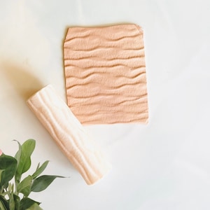 May include: A light brown rolling pin with a wavy texture and a light brown textured square tile.