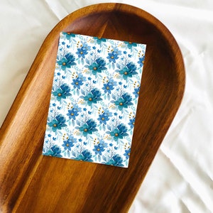 May include: A white card with a blue and gold floral pattern. The card is on a wooden tray.