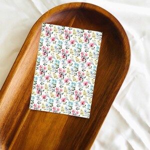 May include: A white card with a floral pattern featuring pink, blue, and yellow flowers on a brown wooden tray.
