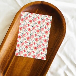 May include: A white card with a pink floral pattern on a wooden tray. The flowers are pink and white with green leaves.