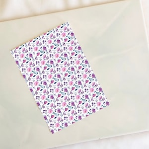 May include: A white sheet of paper with a repeating pattern of purple and pink flowers and leaves.