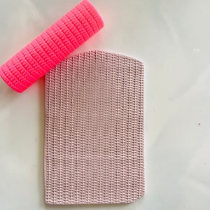 Puede incluir: Un rodillo de silicona rosa con una superficie texturizada y una estera de silicona rosa claro con un patrón tejido.