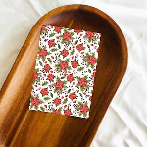 May include: A white card with a red and green floral pattern. The card is on a wooden tray.
