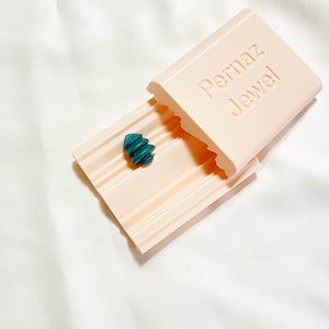 May include: A pink plastic soap dish with a teal soap bar inside. The soap dish has the words "Permaz Jewel" printed on the lid.