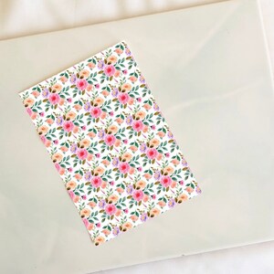May include: A seamless pattern featuring a repeating design of pink, orange, and purple watercolor flowers with green leaves on a white background.