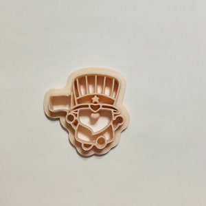 Könnte beinhalten: Ein beiger Plastik-Ausstecher in Form eines Zwergs, der einen Hut mit Sternen und Streifen trägt.