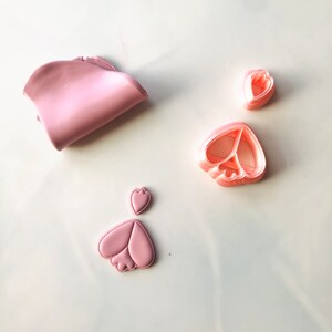 May include: Pink polymer clay and three pink plastic cookie cutters in the shapes of hearts and a flower.