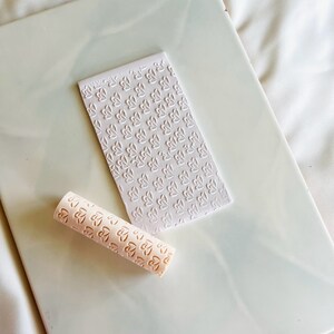 May include: A white rolling pin with a repeating pattern of hearts and a white sheet of paper with the same pattern of hearts.