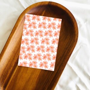 May include: A white card with a repeating pattern of pink watercolor flowers. The card is sitting on a wooden tray.